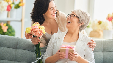 A woman giving her a mother a wrapped gift and flowers